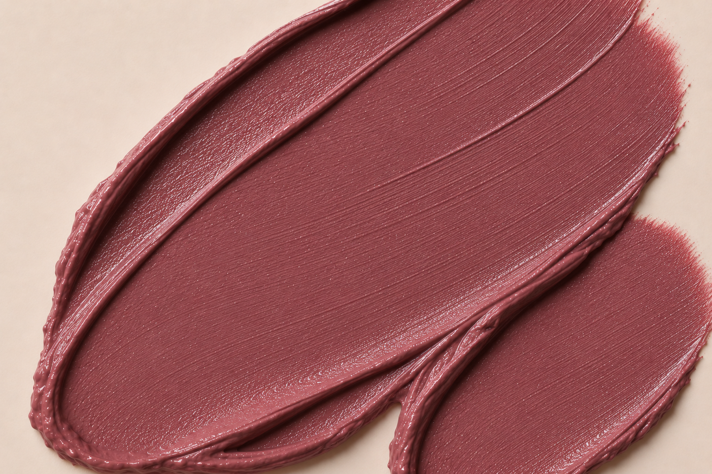 A close-up of a mauve-pink cosmetic cream swatch with visible texture and shading on a light beige background.